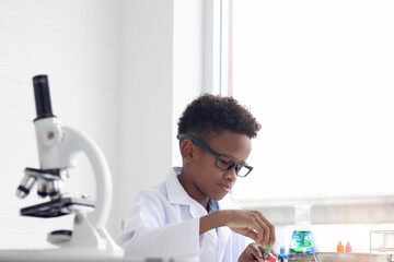 Happy smiling African boy in lab coat doing science experiments, young schoolboy kid scientist...