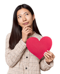 Chinese woman holding Valentine's heart looking sideways with doubtful and skeptical expression.