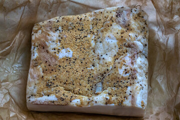 A large piece of lard with garlic and seasonings on parchment paper.