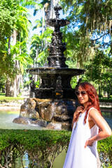 Mujer vestida de blanco junto a fuente de agua en parque