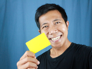 Happy funny face expression Asian man holding empty card on blue background. Transaction concept