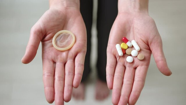 In the frame, two fists open to reveal a condom in one palm and birth control pills in the other. The girl offers us to choose which method of protection we want to use. High quality 4k footage.