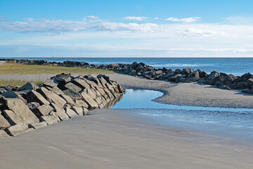 Beach with erosion-control rip-rap and small tidal pool in the foreground and Atlantic Ocean in the background.