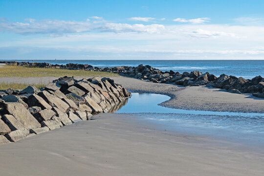 Beach with erosion-control rip-rap and small tidal pool in the foreground and Atlantic Ocean in the background.