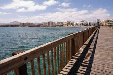 View of the city of Arrecife from the Fermina islet, from a wooden bridge. Turquoise blue water. Sky with big white clouds. Seascape. Lanzarote, Canary Islands, Spain.