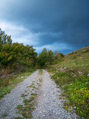 Fototapeta na wymiar Unpaved road under storm clouds through the hilly woodland of the Croatian Mountains.