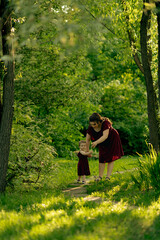 Amid the serenity of nature, a mother and her child take steps together in harmony, a dance of shadows and light playing around them.