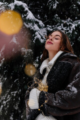 Winter holiday travel, Christmas day, New Year, beautiful happy woman portrait at snowy forest, nature woods, ski resort, leisure activity outdoors, Young Lady enjoying garlands lights in hands