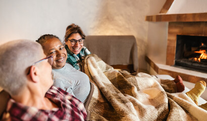 Happy multiracial women having relax in front of fireplace in a cozy house - Winter contents season...