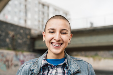 Happy young woman with shaved head smiling in front of camera - obrazy, fototapety, plakaty