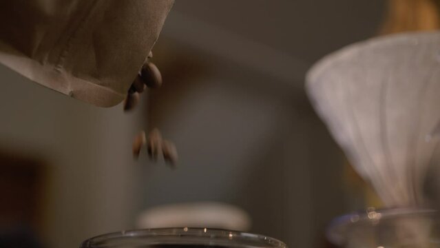 Fresh roasted specialty coffee beans pouring in a grinder by a Barista preparing to grind coffee, making freshly ground coffee
