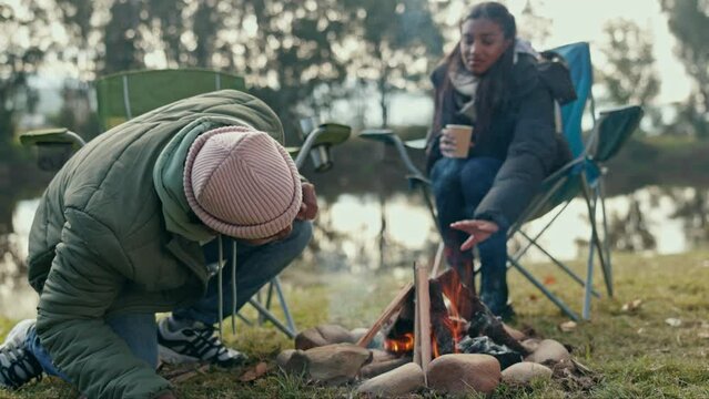 Fire, camping and couple in a forest relax, happy and bond, freedom and travel adventure in nature. Wood, fire and people at camp site with love, coffee and and share exploration experience at lake