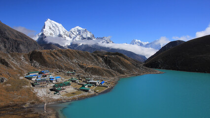 Lodges in Gokyo, turquoise lake Dudh Pokhari and snow covered mountain Cholatse, Nepal.