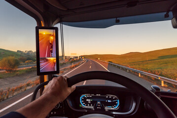 View from inside the cabin of a truck on a highway at dawn, truck with rearview camera and screen.