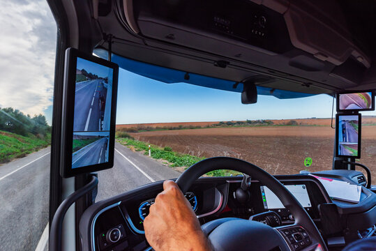 View of the interior of the cabin of a truck with camera mirrors and screens on both sides of the cabin, vehicle traveling on a conventional road.