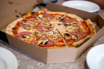 Large pizza cut into pieces in a box on the table. Order food home.