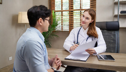 A professional physician in a white medical uniform talks to discuss results or symptoms and gives a recommendation to a male patient and signs a medical paper at an appointment