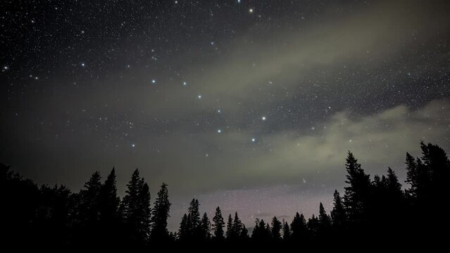 A star filled night sky including the Big Dipper slowly rotates above a skyline of evergreen silhouetted trees in this time lapse video.  The occasional plane and meteor streak through the sky.
