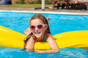 Cute little girl lying on inflatable mattress in swimming pool with blue water on warm summer day on tropical vacations. Summertime activities concept. Cute little girl sunbathing on air mattress