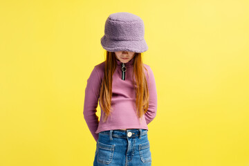 Sad pensive  little girl wearing stylish purple hat and casual clothes looking down. Fashion model...