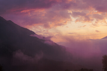 Fog and clouds in the mountains against the backdrop of the setting sun, changeable weather in the mountains, clouds and nebula on mountain peaks wide
