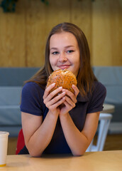 Portrait of young happy woman or beautiful teenager girl eating fast junk food, tasty burger and drink soda in a restaurant or cafe, enjoy meal. 