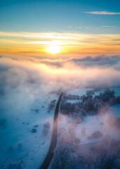 Mountain road going through the snow covered landscape under the low hanging clouds at sunset 