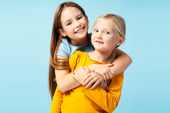 Portrait of smiling girls, cute sisters looking at camera isolated on blue background. Young happy fashion models posing for pictures in studio. Childhood, positive lifestyle concept