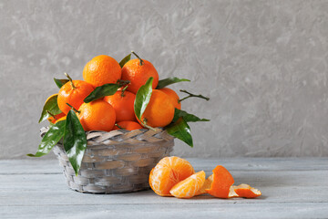 Mandarins fruits in a basket on a wooden table against a gray wall. Beautiful still life, postcard fruits with leaves in a basket on a wooden table near a gray wall. Beautiful still life, postcard