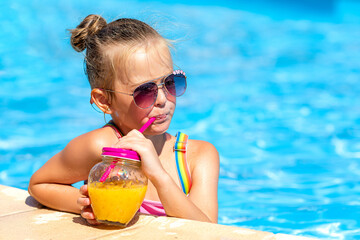 Child drinking juice in swimming pool bar. Summer family vacation with kids. Little girl holding...