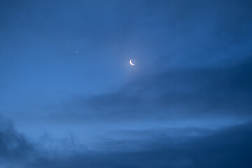 Night sky with old thin bright Moon and star Venus in the clouds, can be used as background.