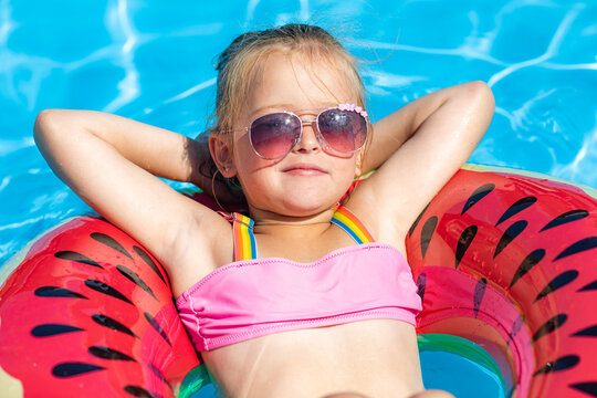 Cute little girl lying on inflatable circle in swimming pool with blue water on warm summer day on tropical vacations. Cute little girl sunbathing on air mattress