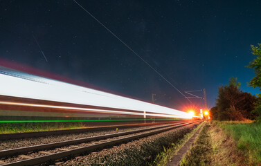 Light trails of a fast driving train at night with the stars of the milky way.