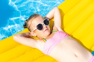 Cute little girl lying on inflatable mattress in swimming pool with blue water on warm summer day on tropical vacations. Summertime activities concept. Cute little girl sunbathing on air mattress - Powered by Adobe