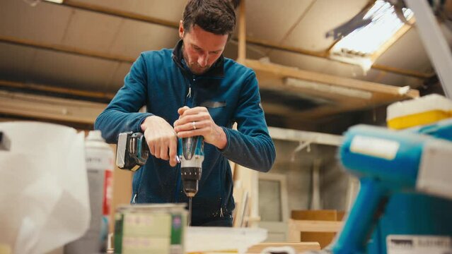 Male carpenter at workbench drilling hole in piece of wood with cordless electric drill - shot in slow motion