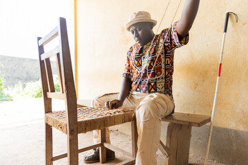 Blind African man sitting, engaged in weaving a dining chair. Blindness and work concept