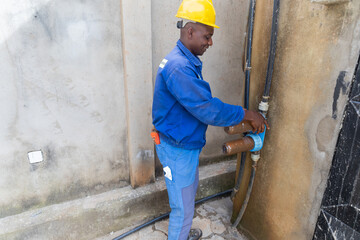 An African blue collar worker preparing to replace dirty rusty water filters - obrazy, fototapety, plakaty