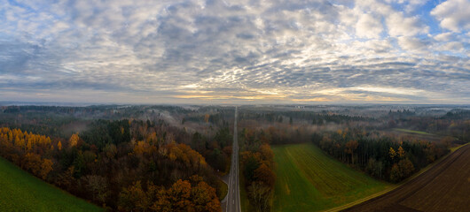 Aerial autumn mist blankets forest and country road.