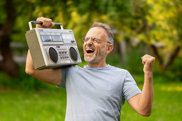 Happy middle aged man listening to retro tape recorder and dancing to his favorite disco song