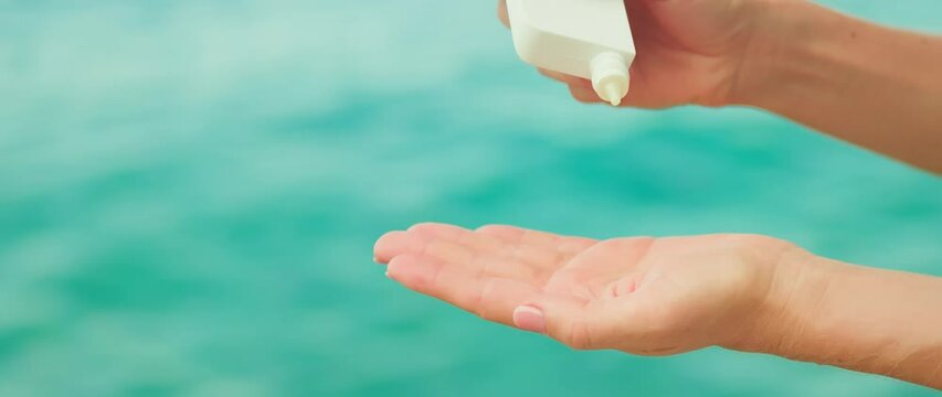 Woman holds a white jar a cosmetic product in hands and dropping liquid into her palm on sea water ripple background. Copy space for text.