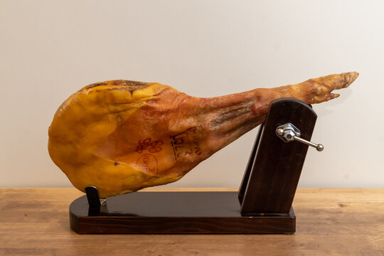 a shoulder of Serrano ham rests in its ham holder ready to start cutting it on a wooden table and a white background