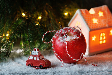Christmas card. A red apple, a toy car with gifts, a candlestick house and coniferous branches of a Christmas tree and pine tree on the table.