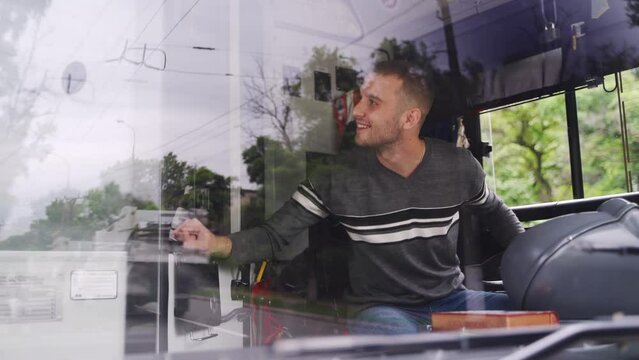 Polite professional transport operator sits on driver's seat, takes fare and gives change and ticket through small window. Young driver in casual clothes receives travel cost from passanger