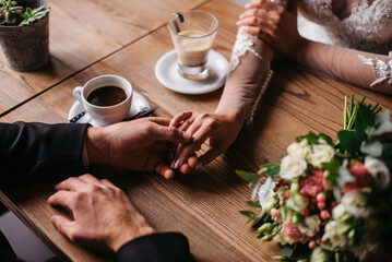 Young beautiful couple in love sitting in a cafe, hugging, touching each other with their hands. Wedding day, celebration, restaurant, coffee shop. The bride and groom drink coffee.