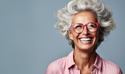 Confident and happy senior woman with stylish gray hair and glasses, smiling broadly, exuding positivity and experience on a light gray background - obrazy, fototapety, plakaty