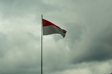 The Indonesian flag, "bendera merah putih", flutters in the gray sky. The concept of sadness or disaster in Indonesia. 