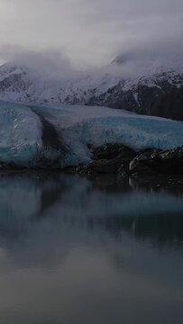 Portage Glacier, Portage Lake, Reflection and Snow-Capped Mountains on Sunny Day. Alaska, USA. Aerial View. Drone Flies Upwards. Vertical Video