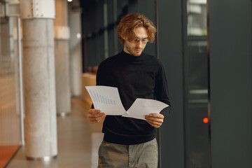 Handsome businessman looking on documents while standing on modern office background