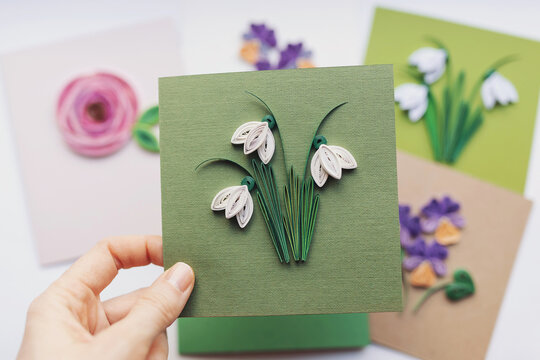 Hand holding quilling card with Snowdrops flowers. woman making greeting cards. Hand made of paper quilling technique. Handicraft at home. Hobby, home office.