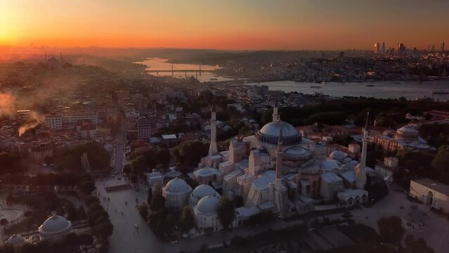 Dome of Hagia Sophia and the Goldenhorn shines in distance at sunset over historic old Istanbul. Chimney smokes from houses rises to sky against bright lights of the sun on a cold winter day
